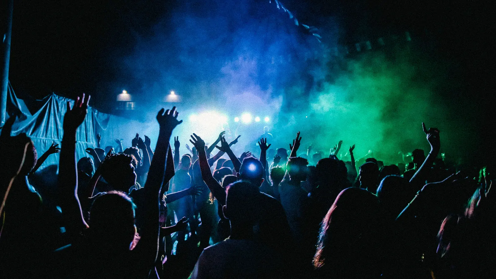 Concert crowd with raised hands under blue and green stage lights