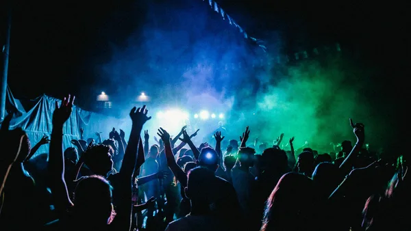 Concert crowd with raised hands under blue and green stage lights